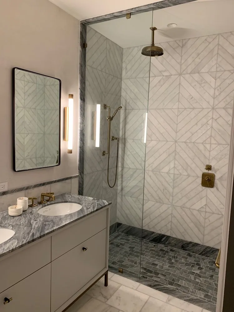 Bathroom by MG Builders with a glass walk-in shower in chevron marble tile and brass fixtures