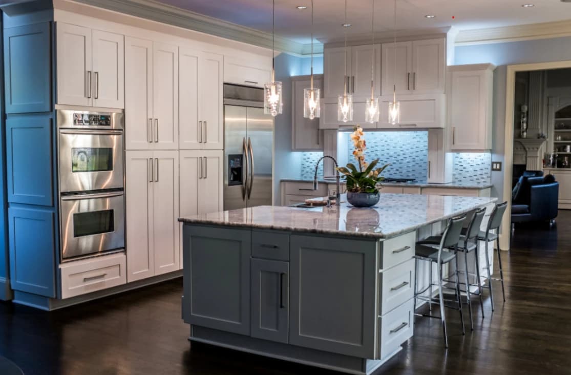 Remodeled kitchen with white shaker cabinets, a gray island with a stone countertop, double wall ovens, and glass pendant lights