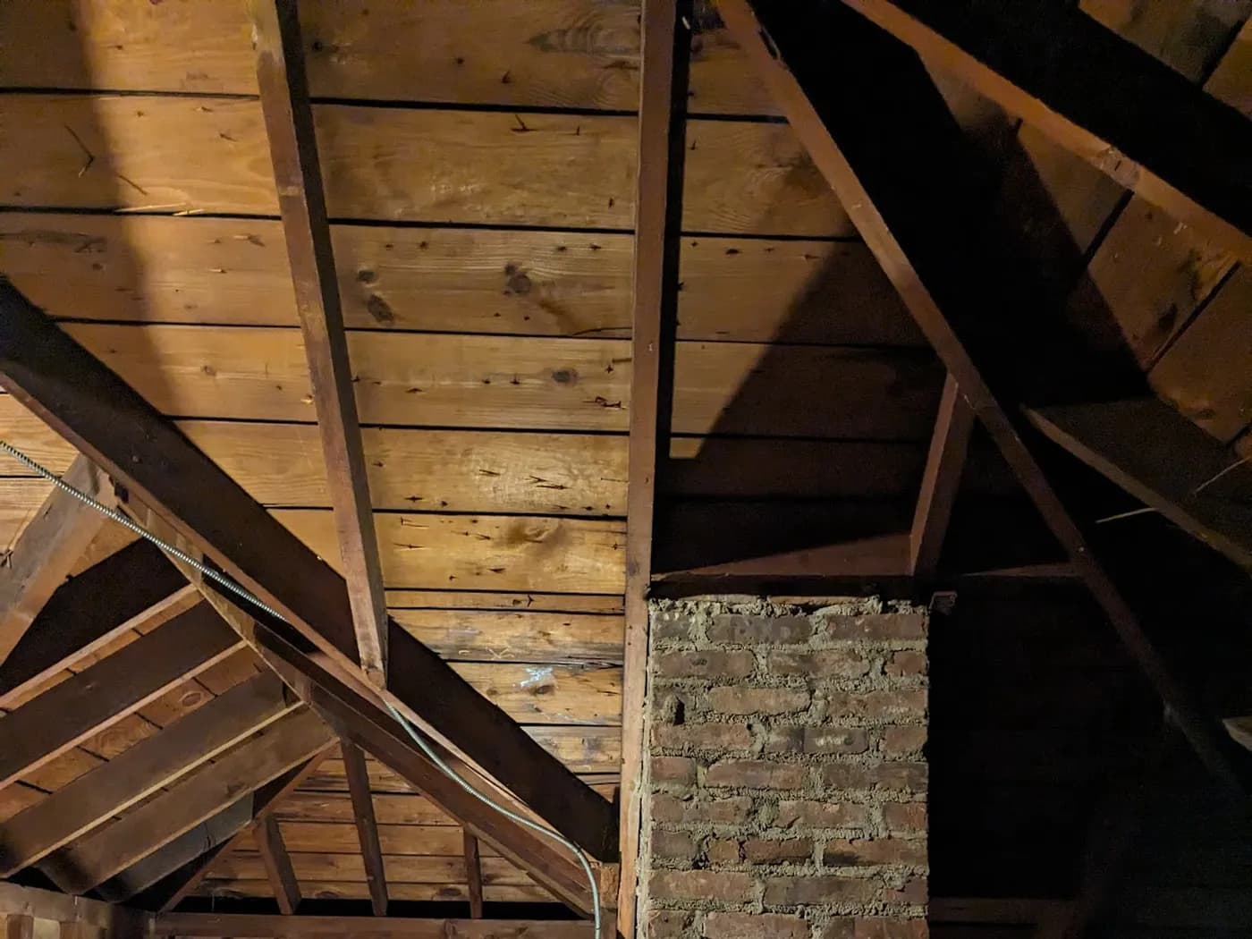 Unfinished attic with exposed rafters, board roof sheathing, a brick chimney and a gable-end window