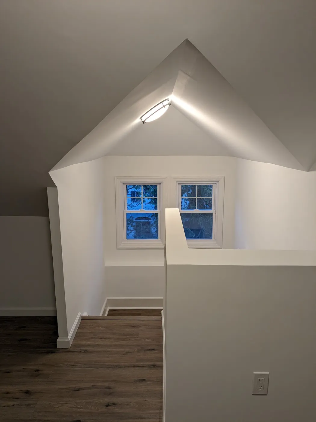 Finished attic with white sloped ceilings, a gable-end window, a ceiling light and wood-look flooring