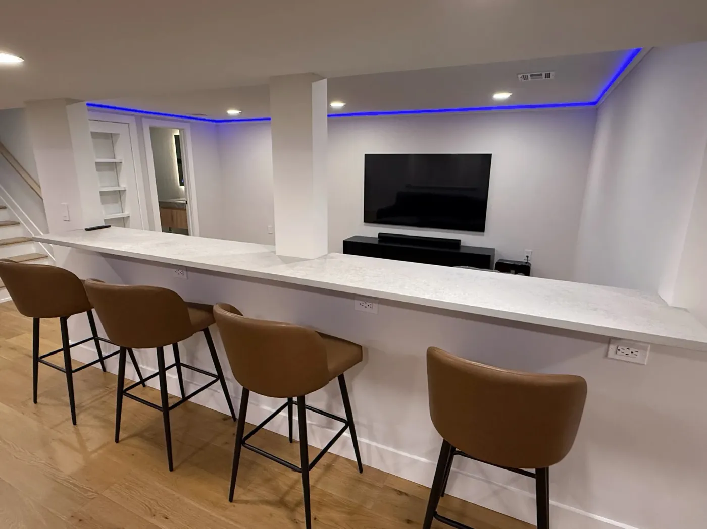 Four bar stools at a long white counter in a finished basement
