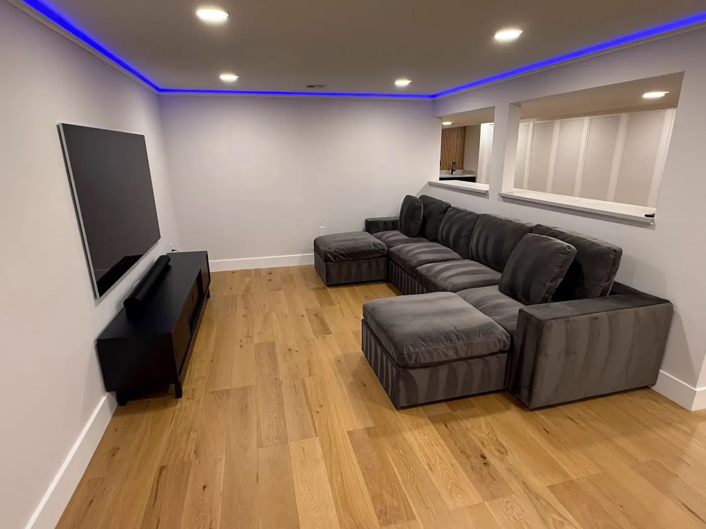 Basement media room with a wall-mounted TV, recessed lights and an LED strip along the ceiling