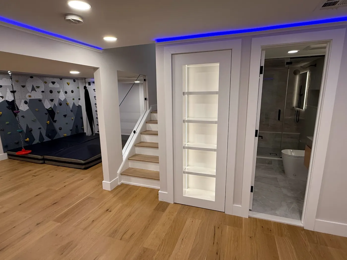 Basement stairs landing at lit white shelves, with the bathroom one step away