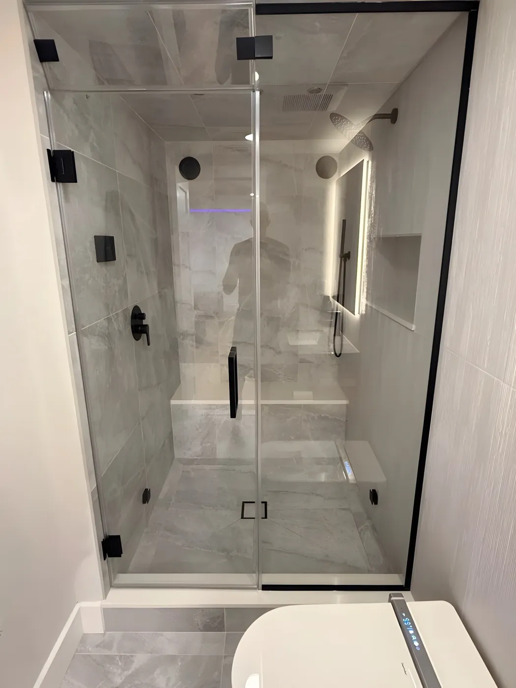 Basement steam shower with frameless glass, gray tile, a built-in bench and matte black fixtures