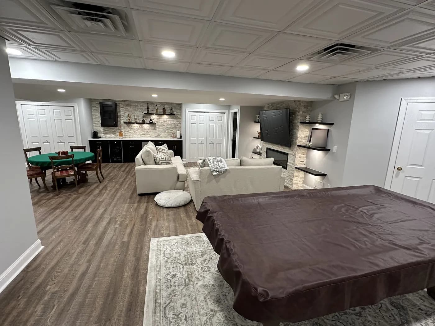 Finished basement recreation room with a covered pool table, sectional seating, stacked-stone fireplace wall and recessed lights