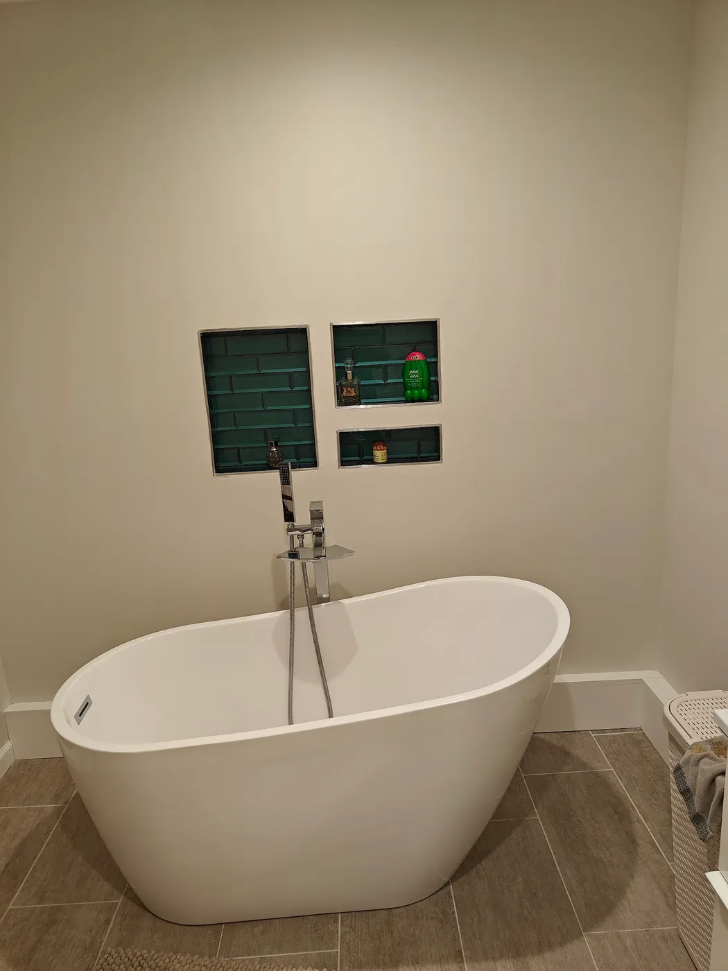 White freestanding soaking tub with a floor-mounted filler below two green-tiled wall niches