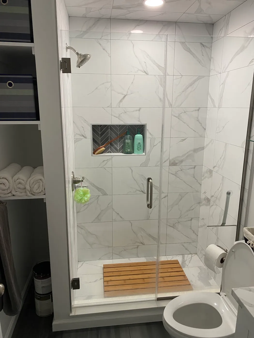 Tiled shower behind a glass enclosure, with a recessed wall niche
