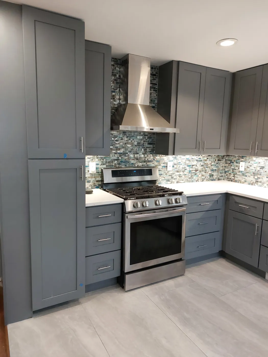 Remodeled kitchen with gray shaker cabinets, a glass mosaic backsplash, a stainless range and a chimney hood