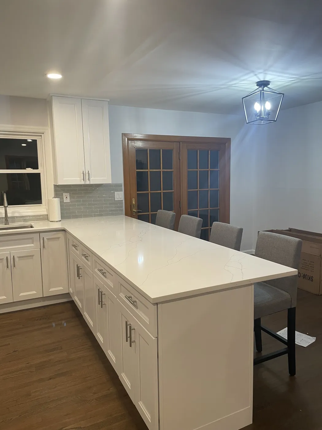 White shaker kitchen with a long peninsula, a light stone countertop, bar stools and wood flooring