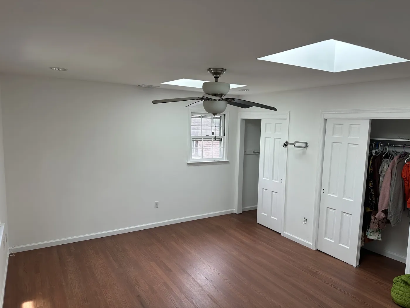 Finished bedroom with two skylights, a ceiling fan, white walls and trim, and wood flooring