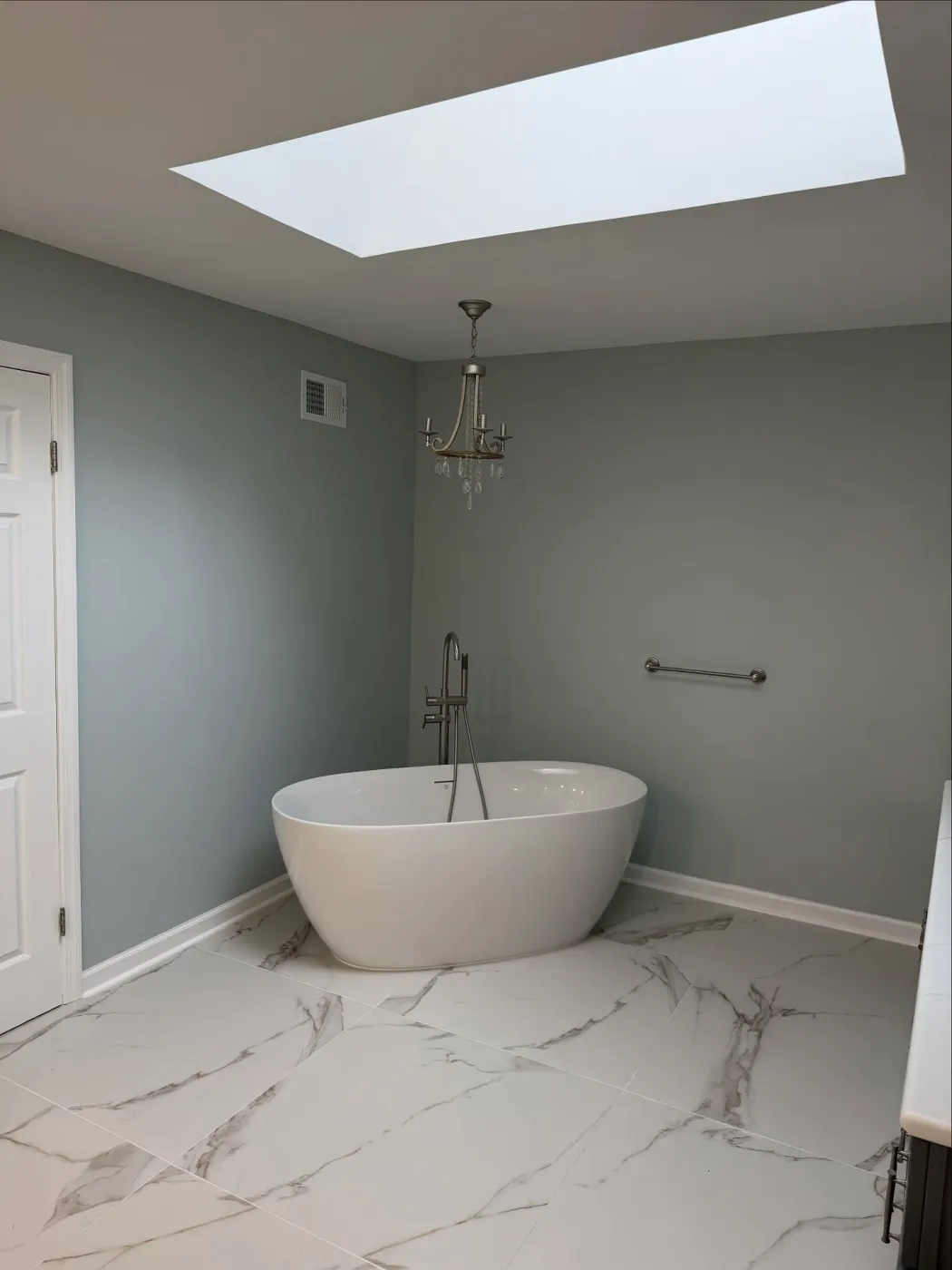 White freestanding tub with a floor-mounted faucet under a bathroom skylight
