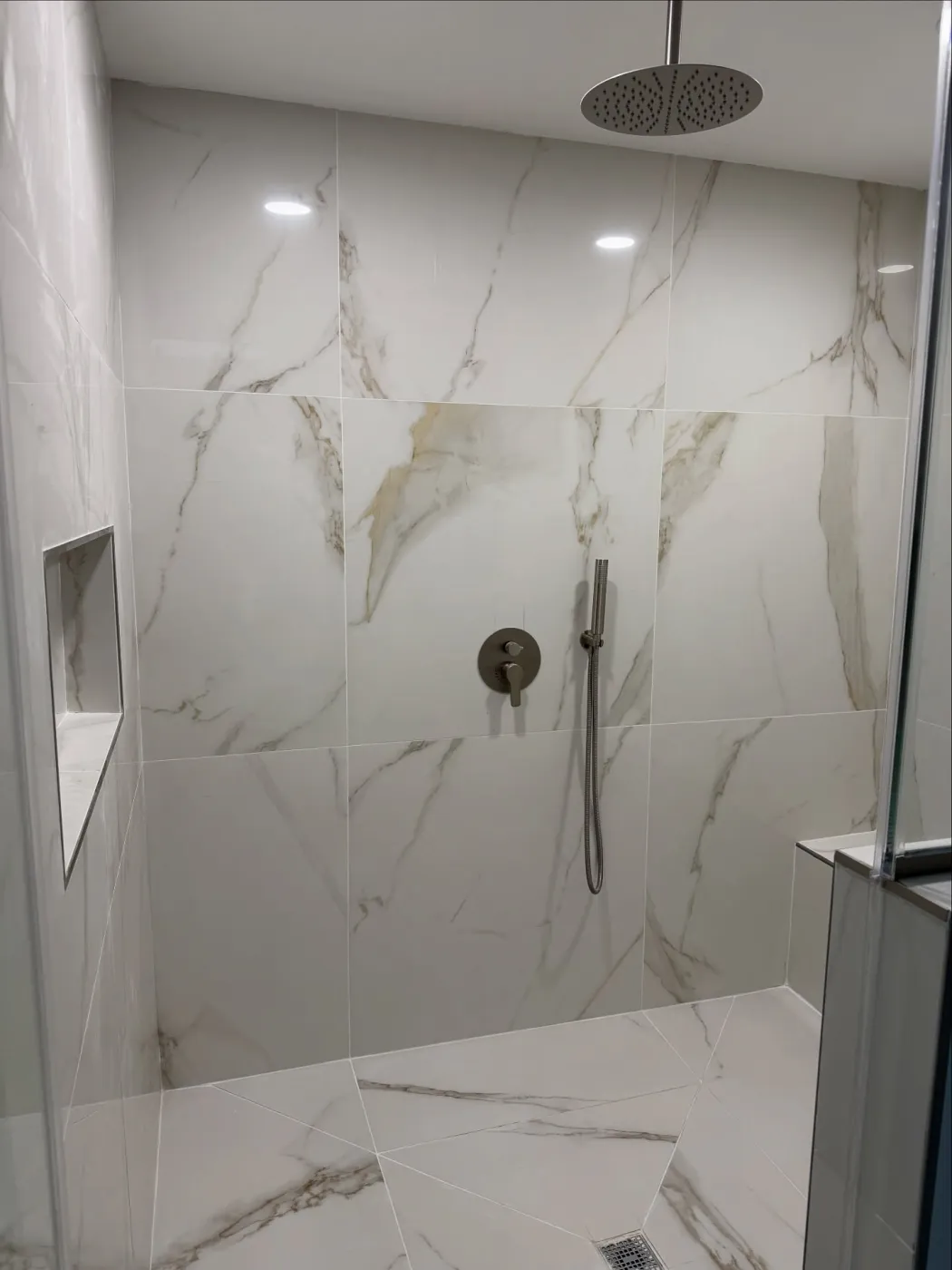 Walk-in shower with large white veined tiles, a ceiling rain head, a hand shower and a wall niche