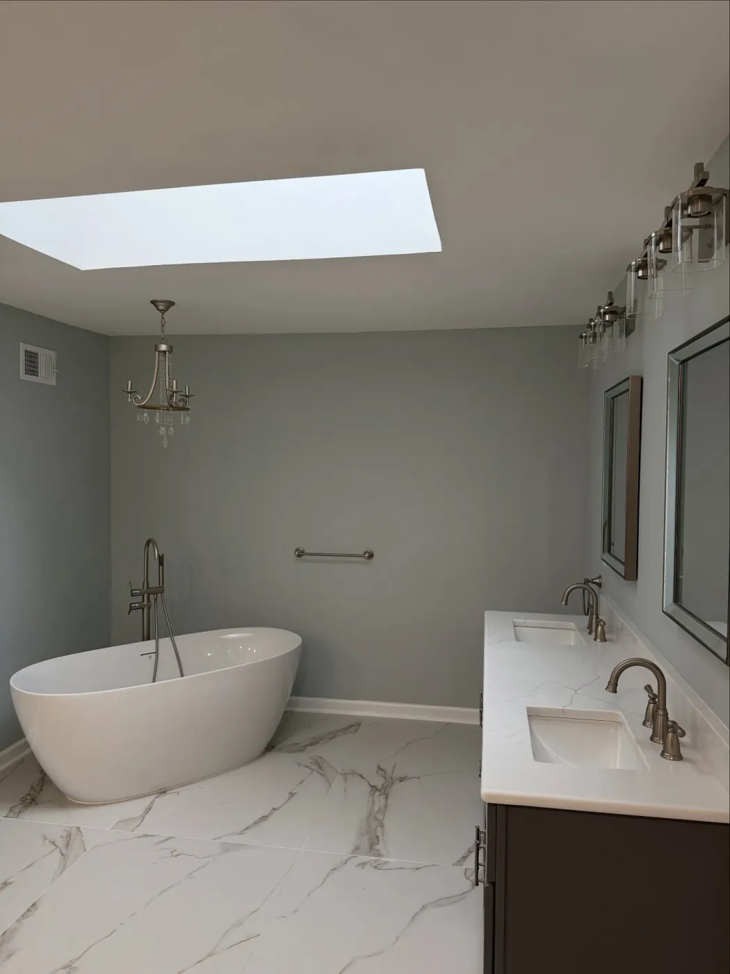 Freestanding tub under the skylight, with the double vanity along the wall beside it