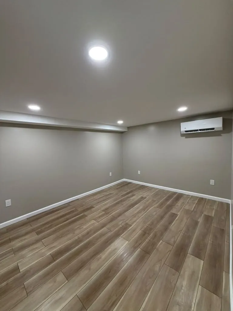 Finished basement room with gray walls, white baseboards, wood-look plank floor, recessed lights and a ductless mini split.