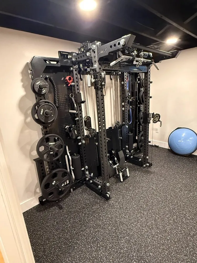 Corner of a finished basement gym with speckled rubber flooring, painted black ceiling and a wall-mounted black weight rack.