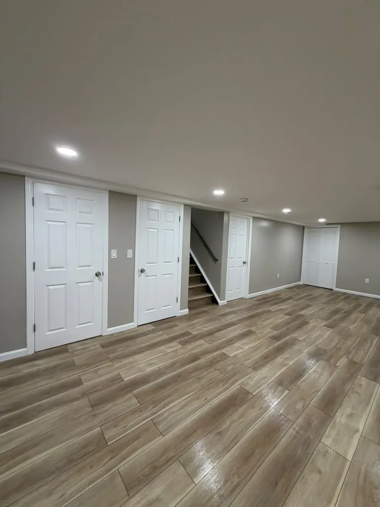 Finished basement with white six-panel doors, a stairway with handrail, louvered closet doors and wood-look plank floor.