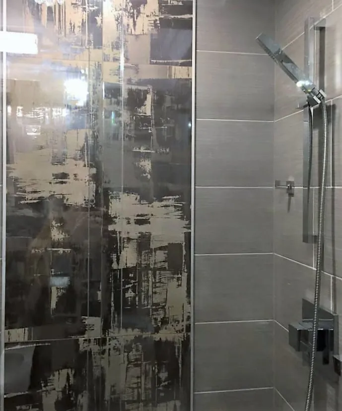 Shower with gray linear tile, a black and gold abstract accent tile panel and handheld shower on a slide bar.