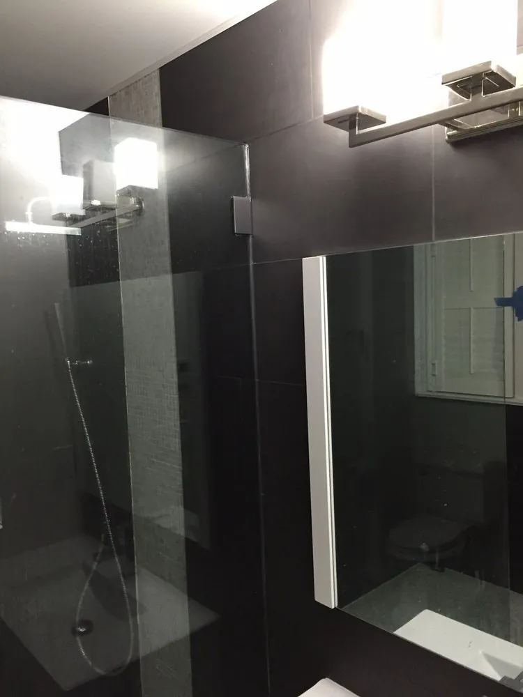Bathroom with large black wall tile, frameless glass shower panel, mosaic accent strip and chrome vanity light over a mirror.