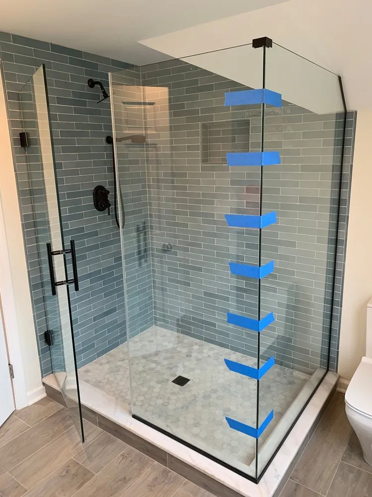 Glass shower with blue-gray glass subway tile, matte black fixtures and hardware, and marble hexagon floor.