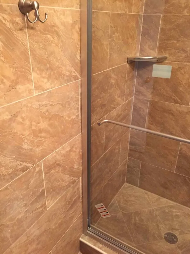 Shower with brown marble-look porcelain tile set in a staggered pattern, framed glass door, towel bar and corner shelf.