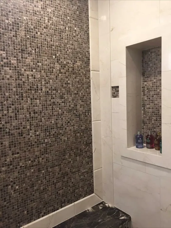 Shower with a brown marble mosaic accent wall, cream tile, tall niche and dark granite bench.