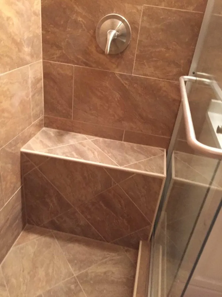 Tiled shower bench in brown marble-look porcelain set on the diagonal, brushed nickel valve and sliding glass door.