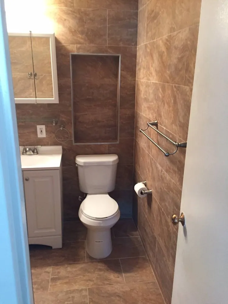 Small bathroom with brown marble-look porcelain walls and floor, recessed wall niche, white vanity and toilet.