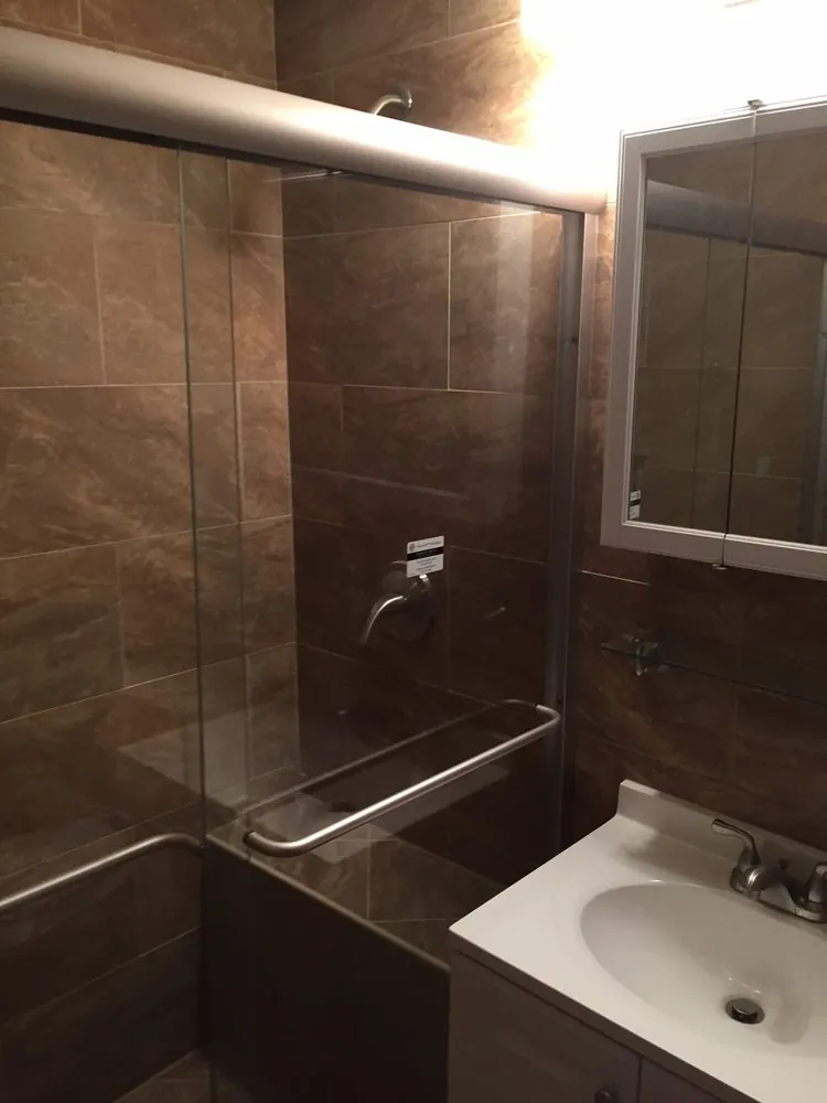 Tub shower with brown marble-look tile, sliding glass doors and a white vanity with medicine cabinet.