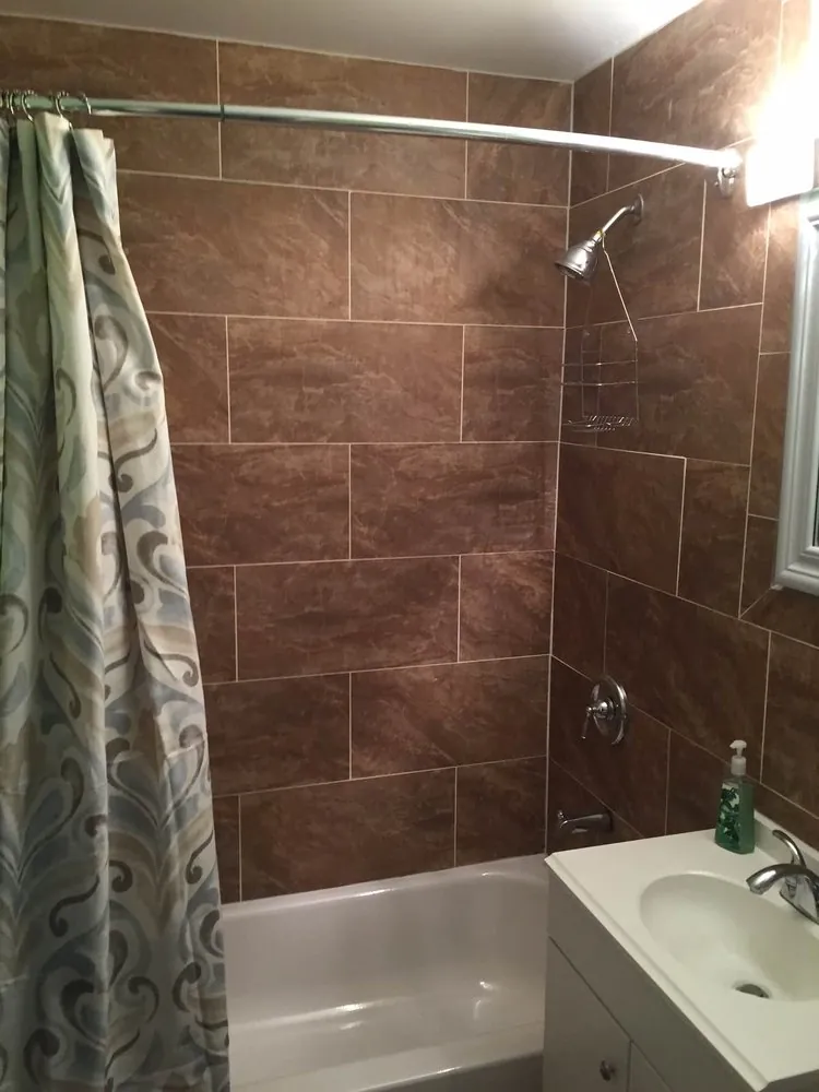 Tub with brown marble-look tile surround, curved shower rod and curtain, and a white vanity.