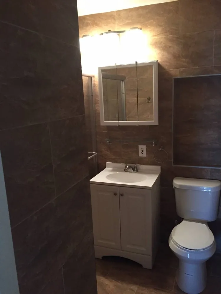 Bathroom with brown marble-look wall and floor tile, white vanity, medicine cabinet and toilet.