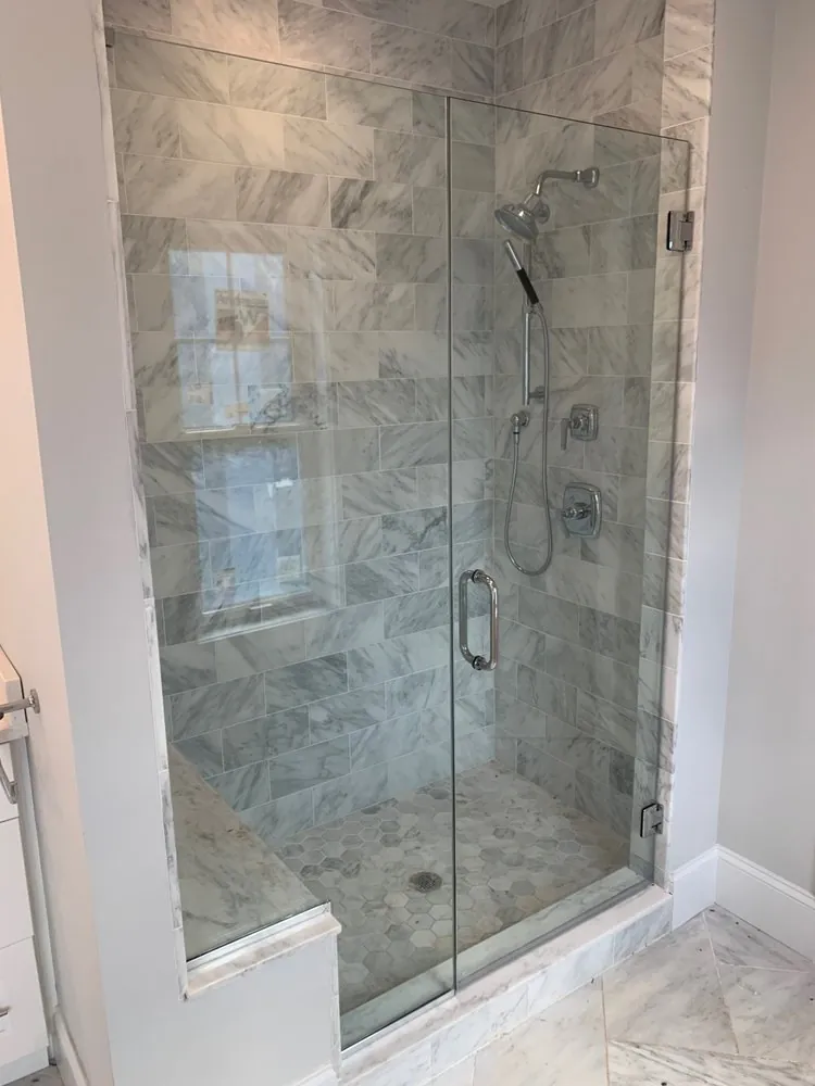 Glass shower with white Carrara marble wall tile, marble hexagon floor, corner bench and chrome handheld shower.