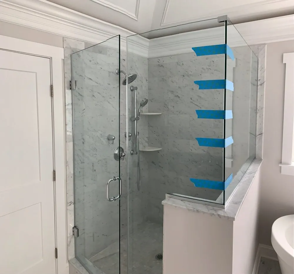 Glass shower enclosure on a marble-capped knee wall, Carrara marble walls, chrome rain head and hand shower.