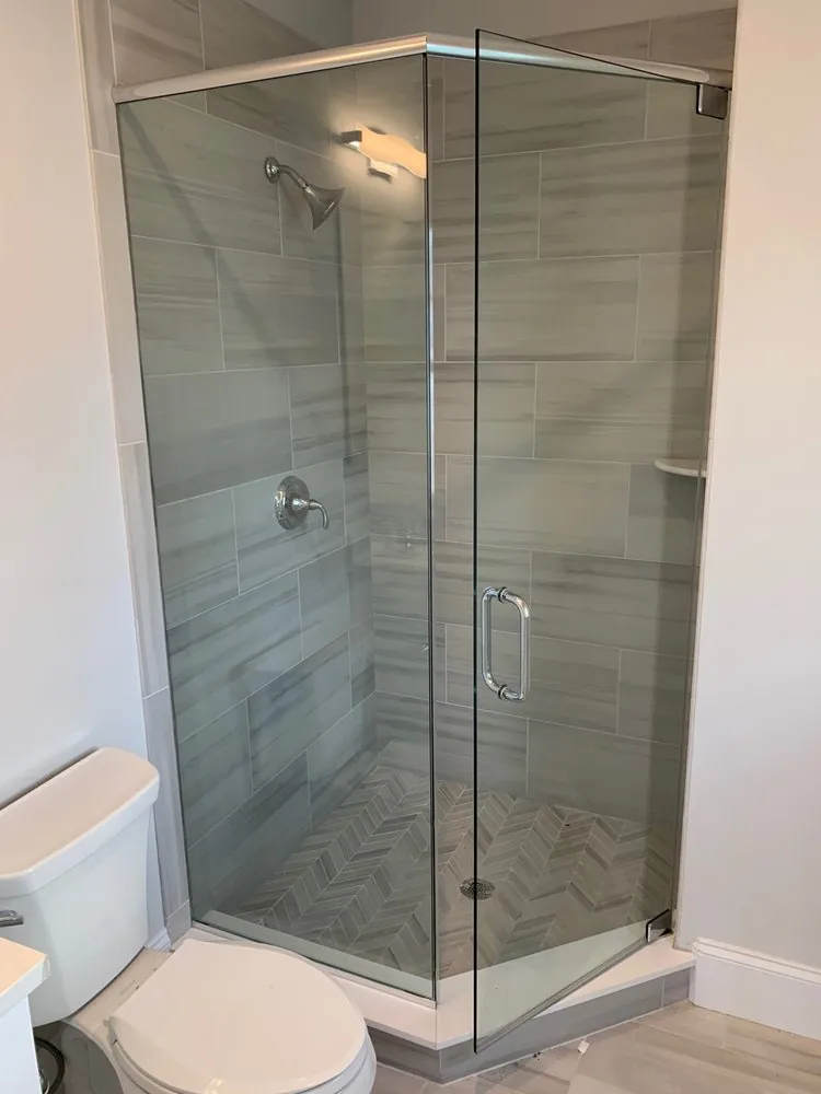 Corner glass shower with gray linear plank tile on the walls and a gray chevron tile floor, chrome fixtures and toilet.