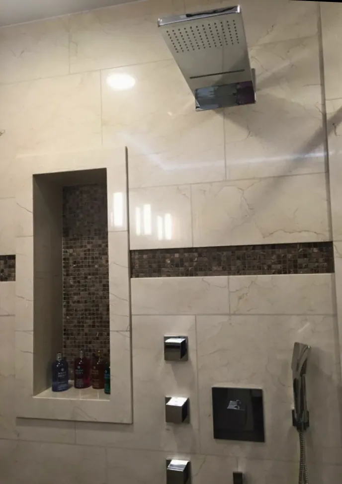 Shower with cream marble-look tile, brown mosaic band and niche, rectangular rain head and body sprays.
