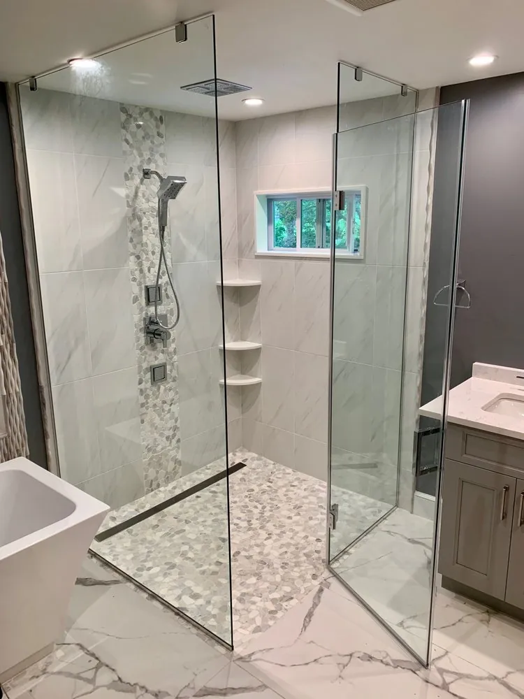 Curbless glass shower with white marble-look tile, pebble accent strip and floor, linear drain and freestanding tub.