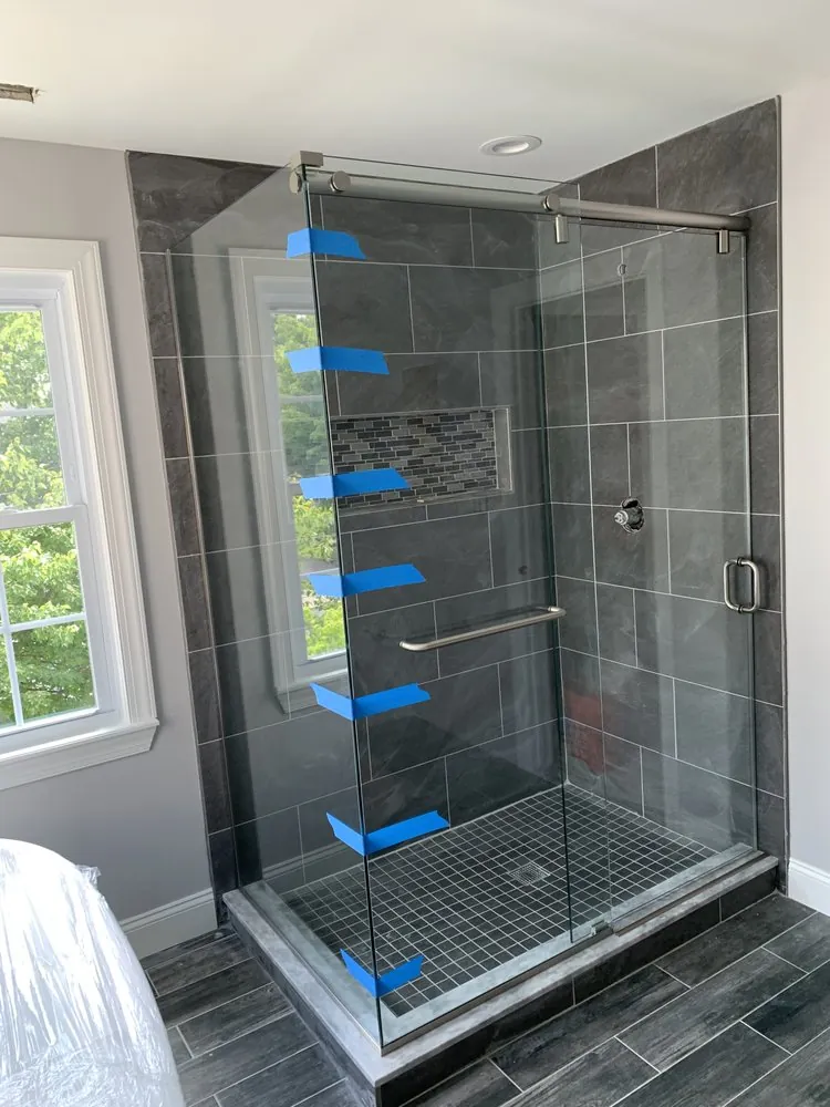 Shower with dark gray slate-look tile, mosaic niche, small square floor tile and a new sliding glass door.