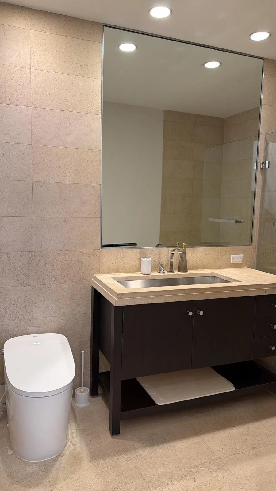 Dark wood open-shelf vanity with beige stone top and undermount steel sink, large wall mirror and white smart toilet.