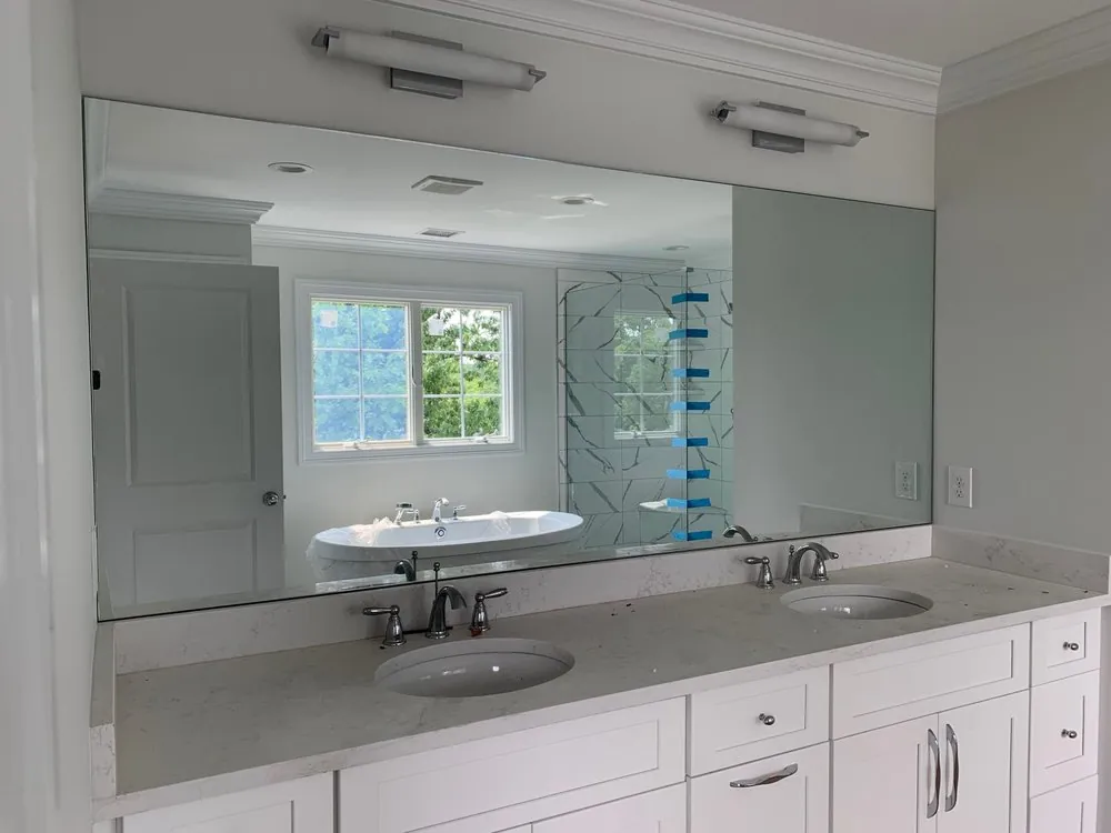 White shaker double vanity with quartz top, two undermount sinks, a wide frameless mirror and two bar lights.