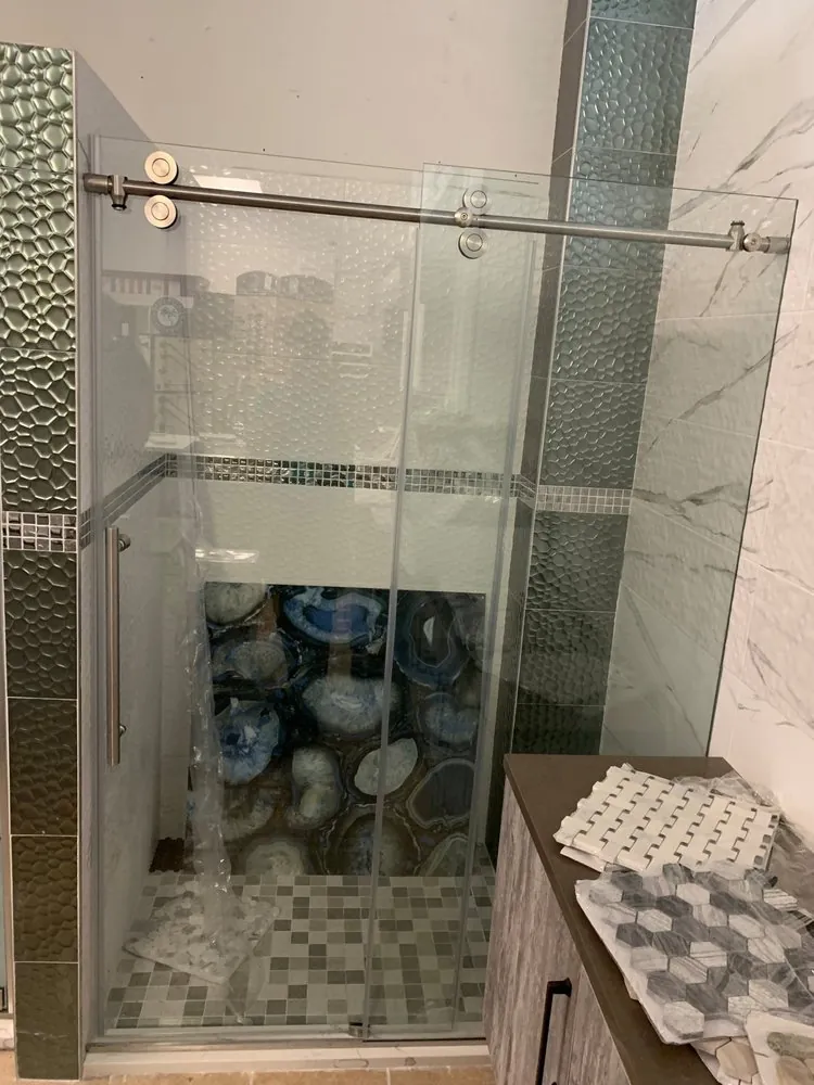 Sliding glass shower door in progress, textured silver tile, blue agate accent wall and mosaic floor, tile samples nearby.
