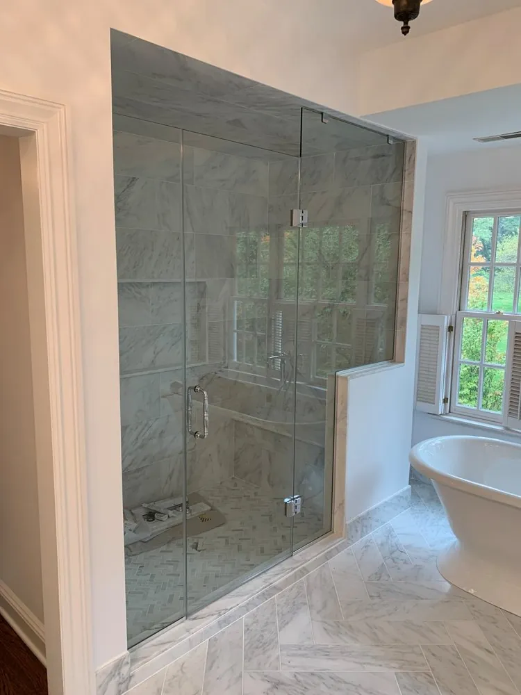 Marble steam shower with frameless glass and herringbone floor beside a freestanding tub and herringbone marble floor.