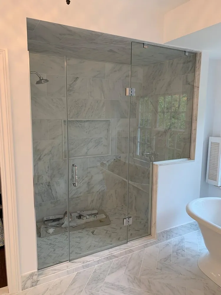 Marble steam shower with frameless glass, herringbone floor and half wall, supplies still inside, tub beside it.