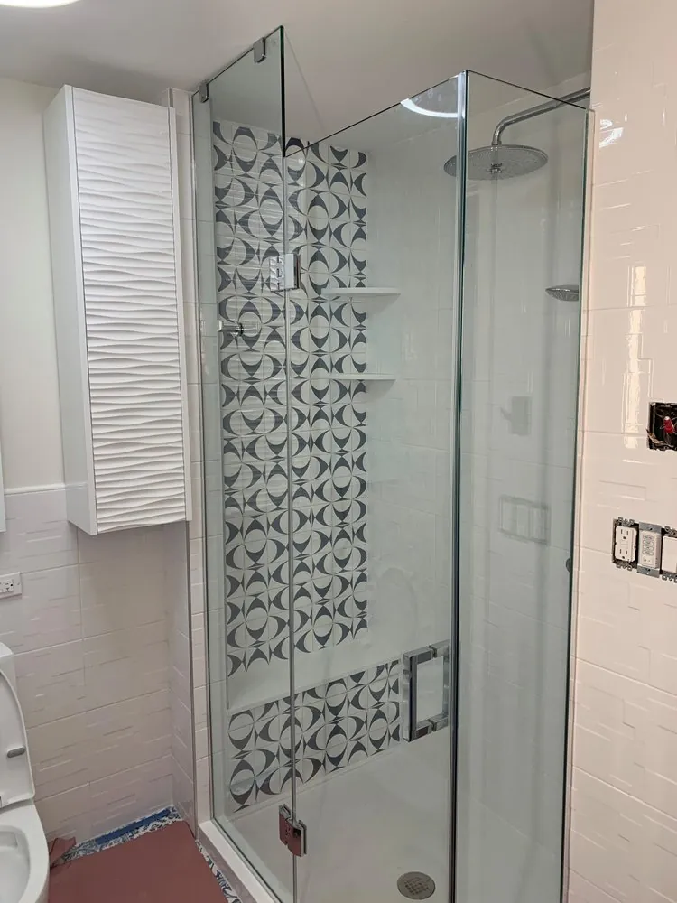 Frameless glass shower with navy and white geometric accent tile, white subway walls, rain head and a wave-front cabinet.