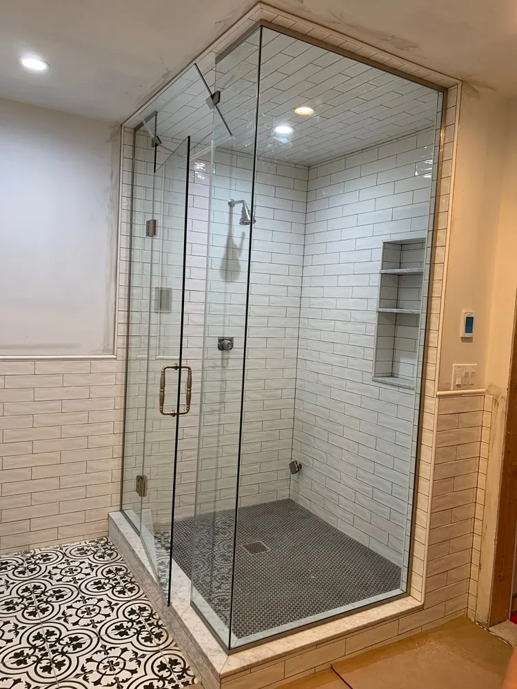 Glass shower with white subway tile on walls and ceiling, gray penny floor and niche, beside black and white patterned tile.