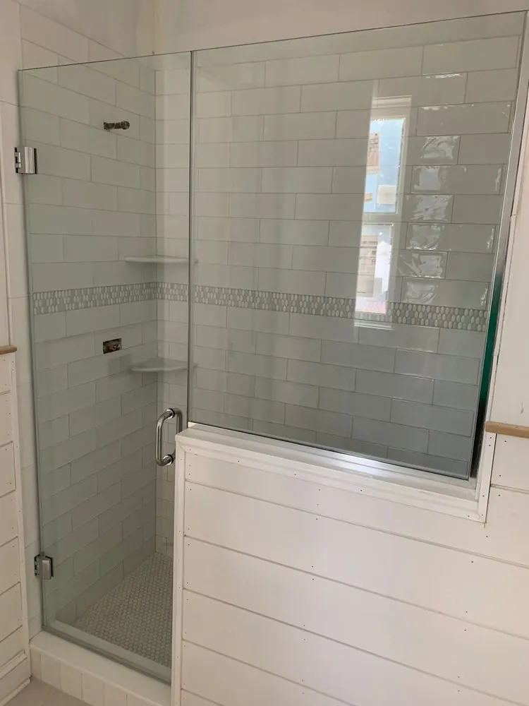 Glass shower being finished, white subway tile with pebble mosaic band, corner shelves and a white shiplap knee wall.