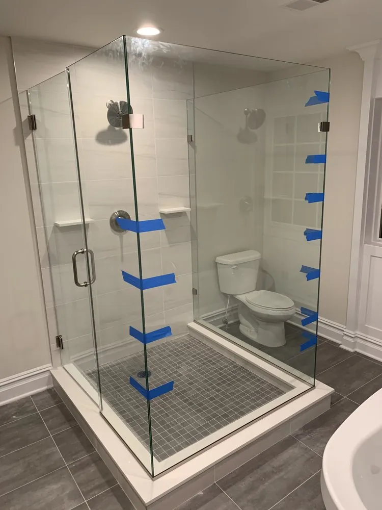 Frameless glass shower enclosure with light gray wall tile and gray mosaic floor on a white curb, glass just installed.