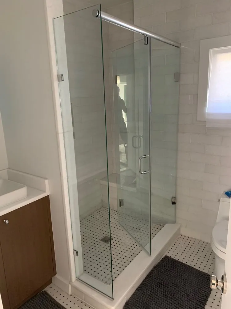 Frameless glass shower with white stone tile, built-in bench and white mosaic floor with black dots, beside a wood vanity.