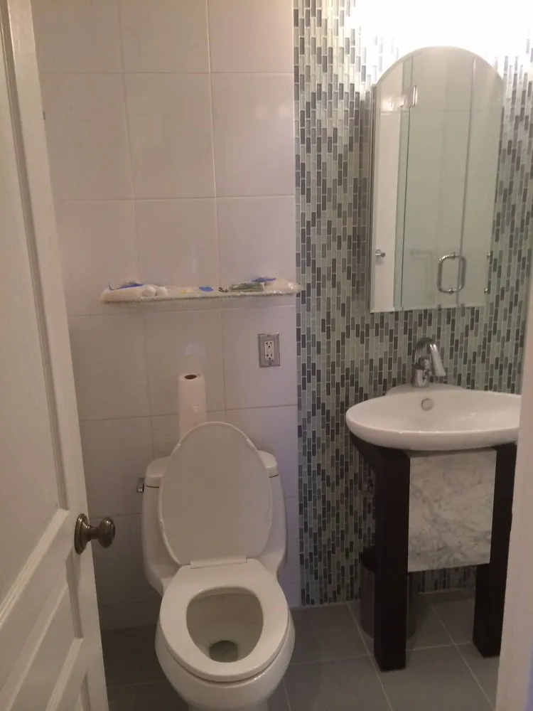 Bathroom with white wall tile, blue-green glass mosaic accent wall, oval sink on dark stand, arched mirror and toilet.