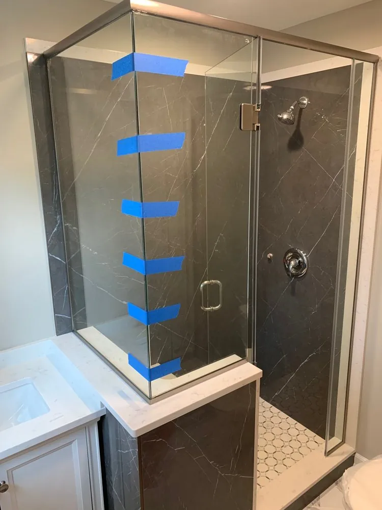 Frameless glass corner shower with charcoal marble-look walls, white mosaic floor and a white vanity with quartz top.