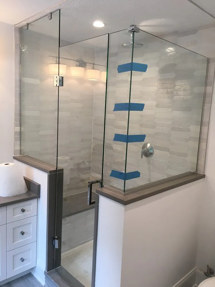 Frameless glass shower on a knee wall with gray cap, white elongated hexagon tile and rain head.