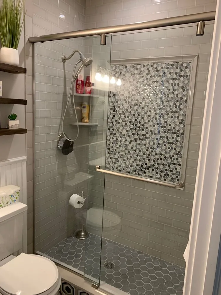 Sliding glass shower door, gray glass subway tile, framed gray hex mosaic panel and gray hex floor.